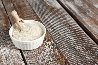 Photo of Raw basmati rice in bowl and scoop on wooden table, space for text