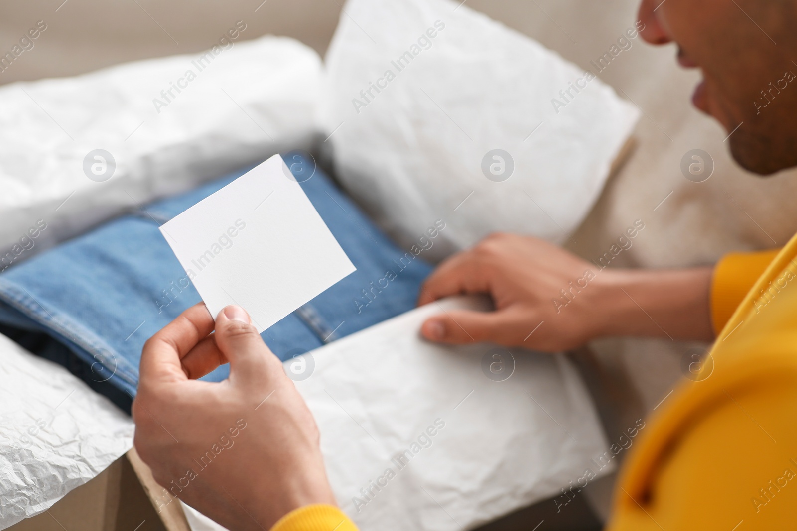 Photo of Young man holding greeting card near parcel with Christmas gift, closeup