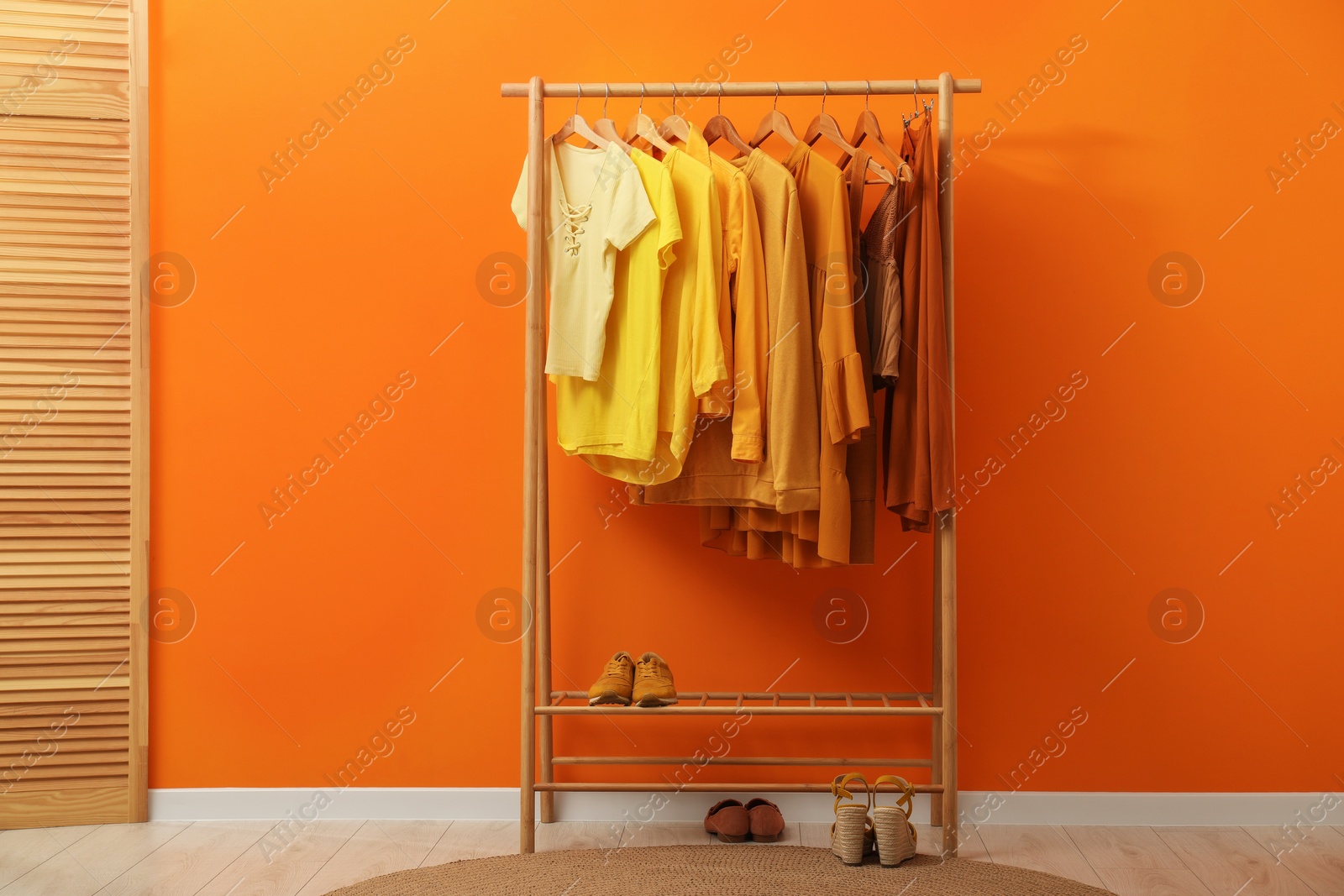 Photo of Rack with different stylish women's clothes, shoes and wooden folding screen near orange wall indoors