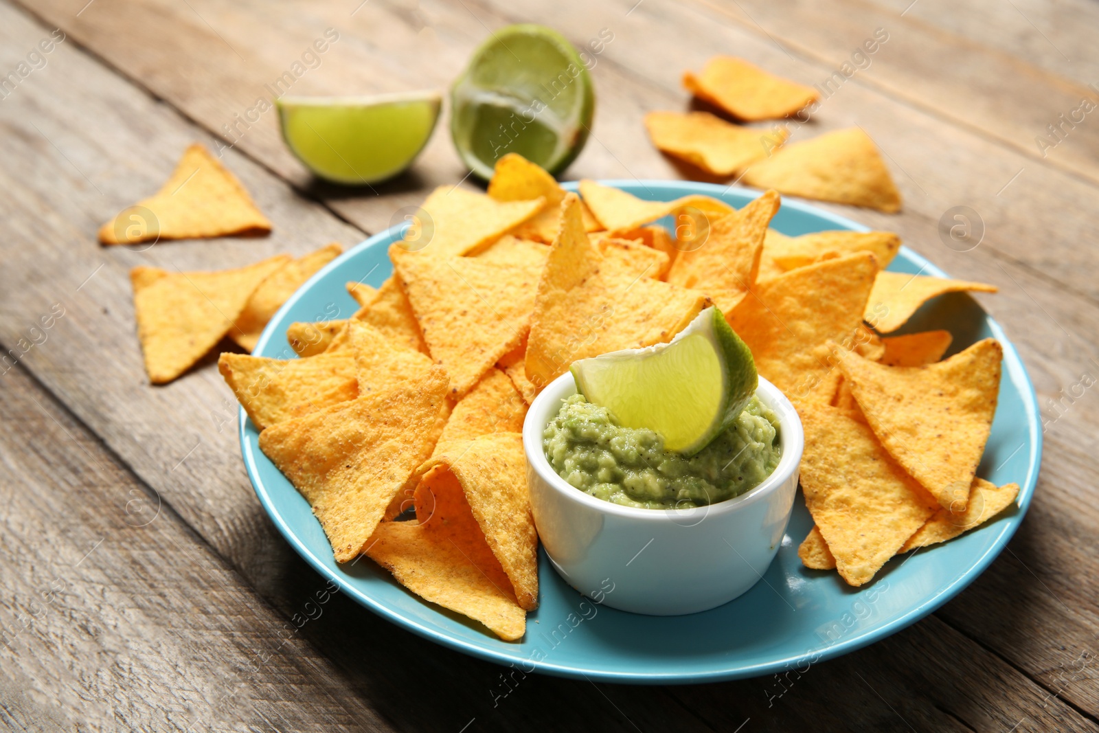 Photo of Plate with delicious mexican nachos chips, guacamole sauce and lime on wooden table