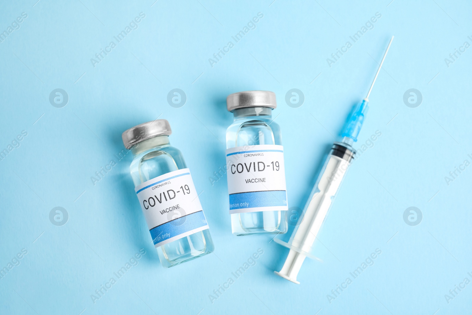 Photo of Vials with coronavirus vaccine and syringe on light blue background, flat lay