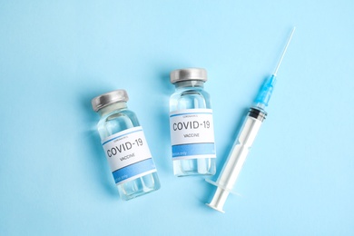 Vials with coronavirus vaccine and syringe on light blue background, flat lay