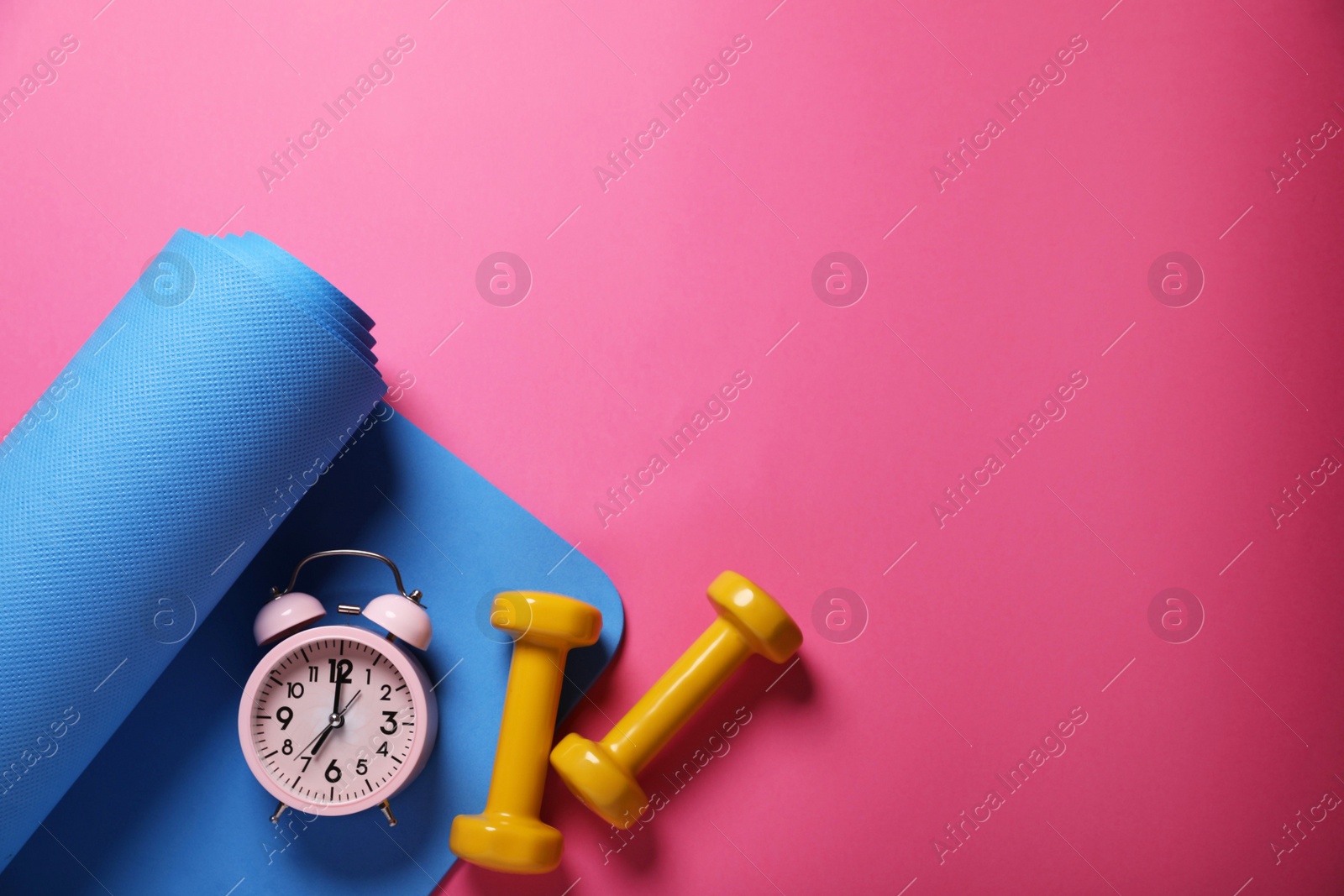 Photo of Fitness mat, dumbbells and alarm clock on pink background, flat lay with space for text. Morning exercise