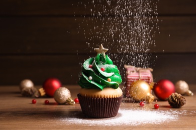 Sprinkling powdered sugar on Christmas tree shaped cupcake