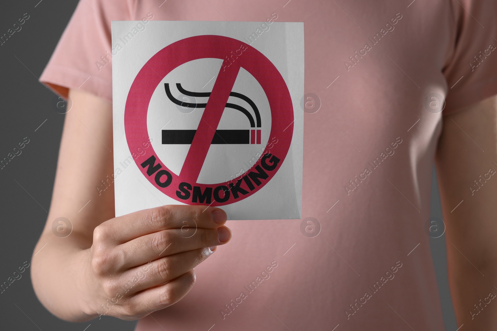 Photo of Woman holding card with no smoking sign on gray background, closeup