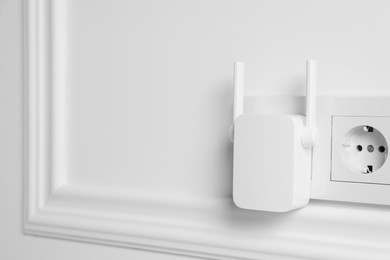 Wireless Wi-Fi repeater on white wall, space for text