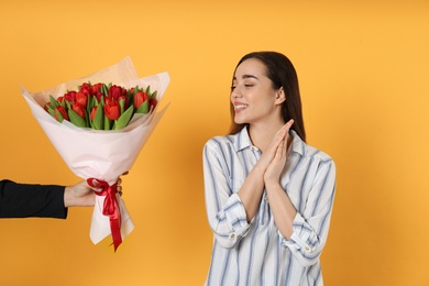 Photo of Happy woman receiving red tulip bouquet from man on yellow background. 8th of March celebration