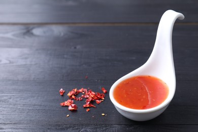 Photo of Chili sauce in spoon on black wooden table, closeup. Space for text