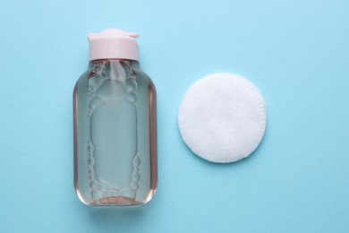 Photo of Micellar water and cotton pad on light blue background, flat lay