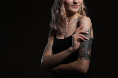 Photo of Beautiful woman with tattoos on body against black background, closeup. Space for text