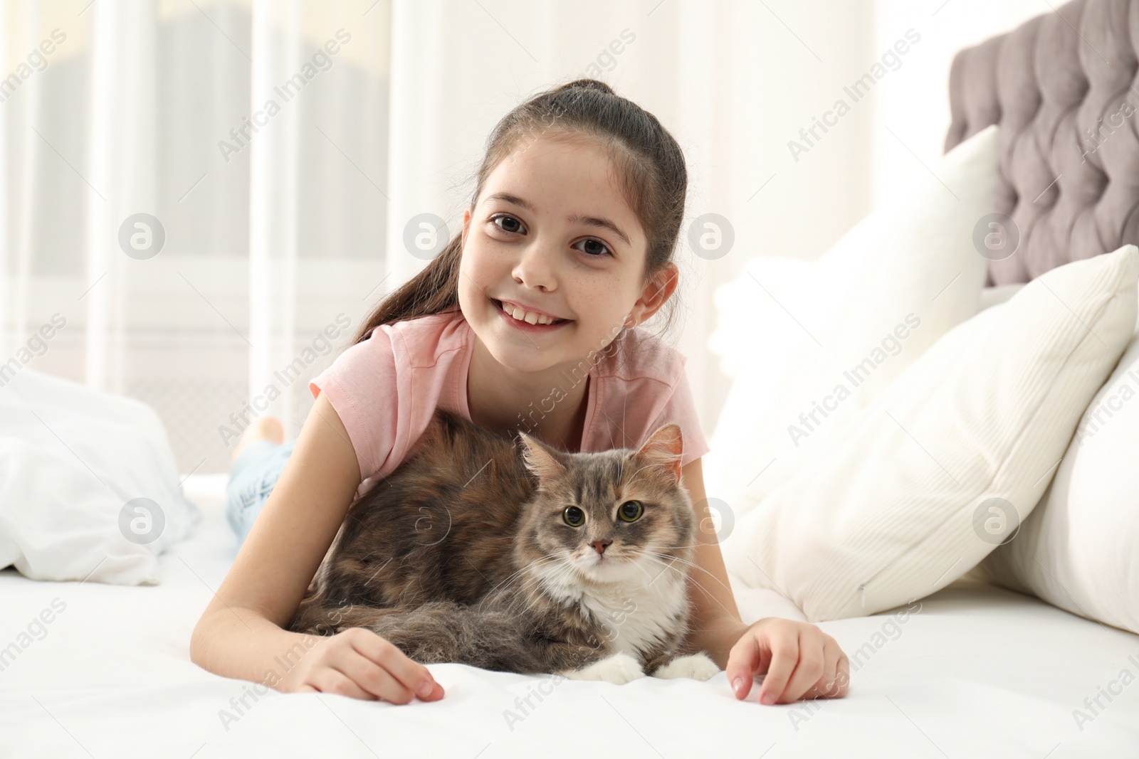 Photo of Cute little girl with cat lying on bed at home. First pet