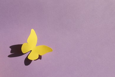 Yellow paper butterfly on violet background, top view. Space for text