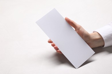 Woman holding blank card at white table, closeup. Mockup for design