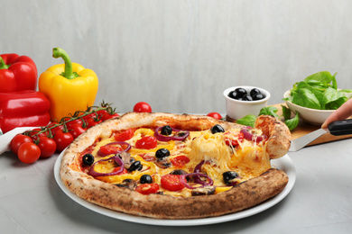 Woman taking slice of tasty vegetable pizza at light grey table, closeup