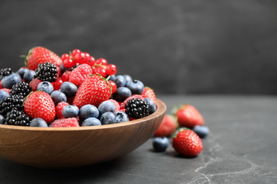 Mix of different fresh berries in bowl on grey table. Space for text