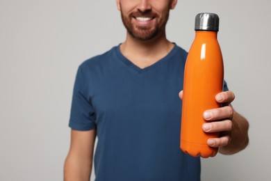 Man with orange thermo bottle against light grey background, closeup. Space for text