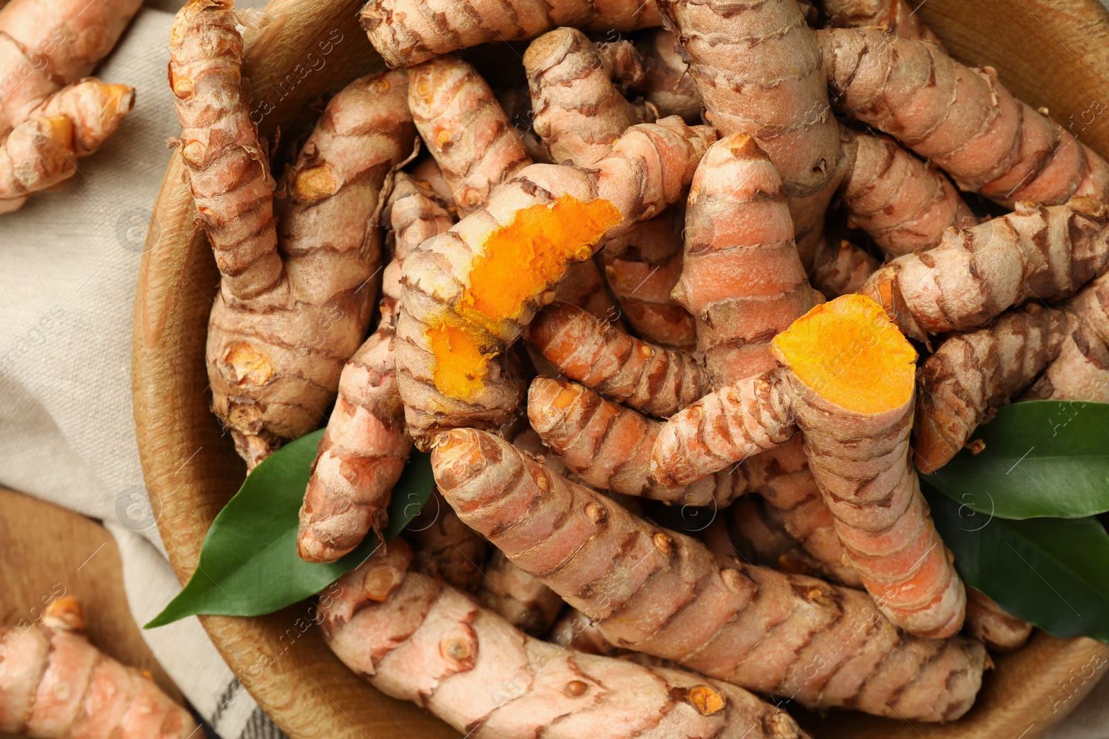 Photo of Many raw turmeric roots and green leaves on table, flat lay