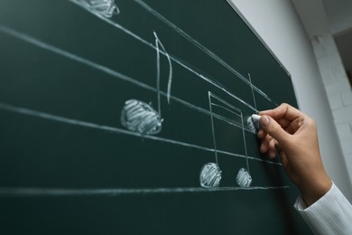 Photo of Teacher writing music notes with chalk on greenboard, closeup