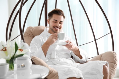 Handsome young man drinking tea in spa salon