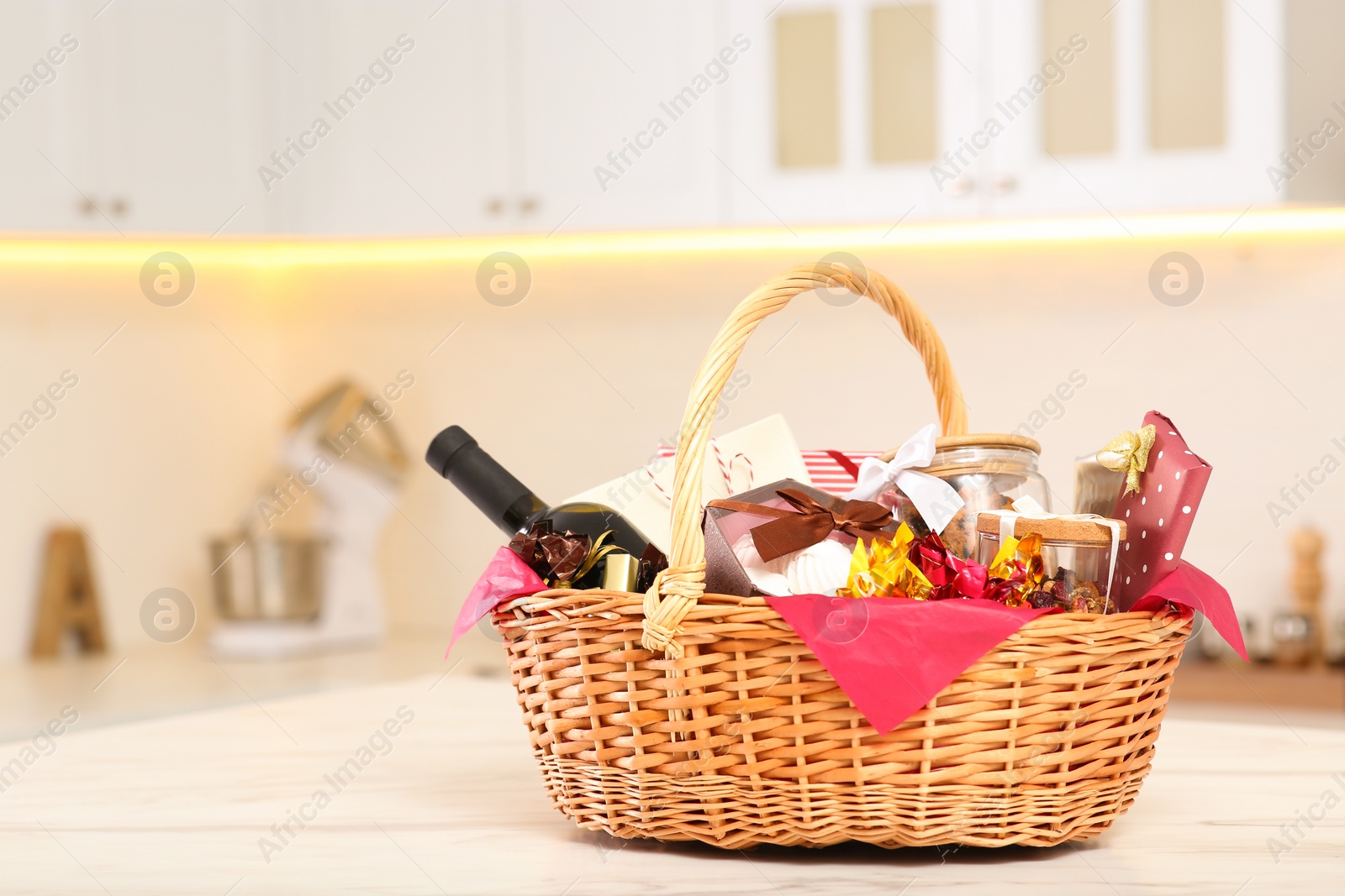 Photo of Wicker basket full of gifts on wooden table in kitchen. Space for text