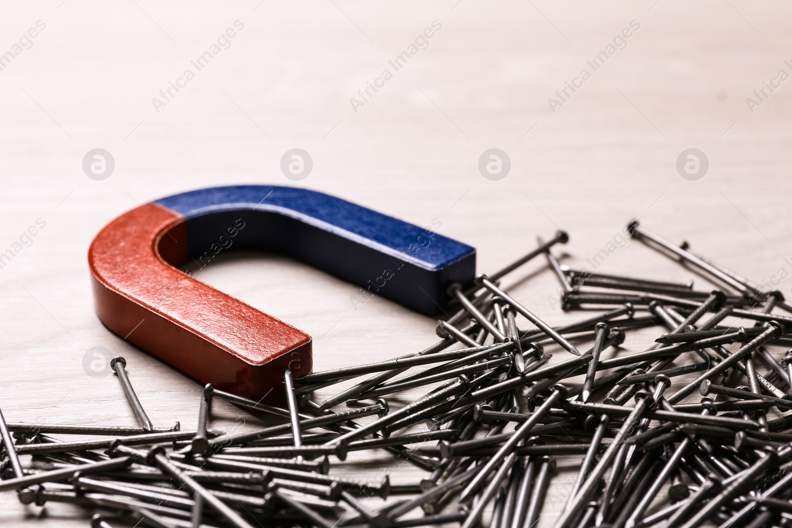 Photo of Magnet attracting nails on light wooden background, closeup