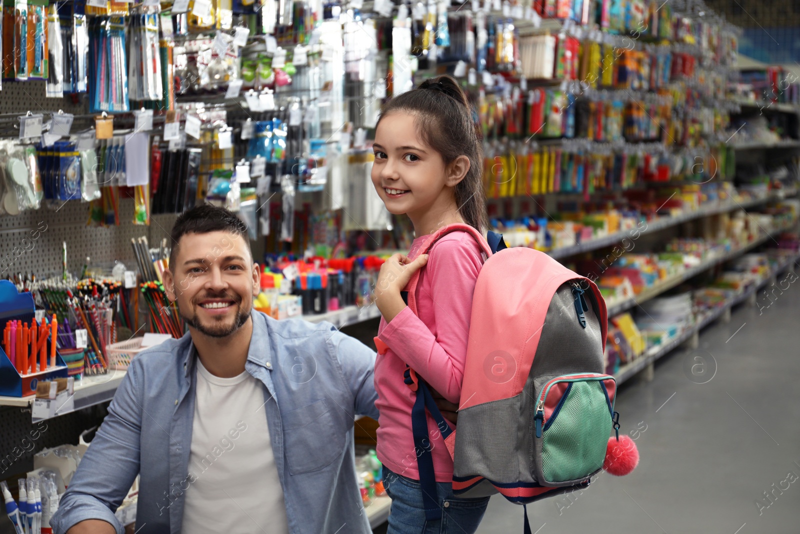 Photo of Little girl with father choosing school stationery in supermarket