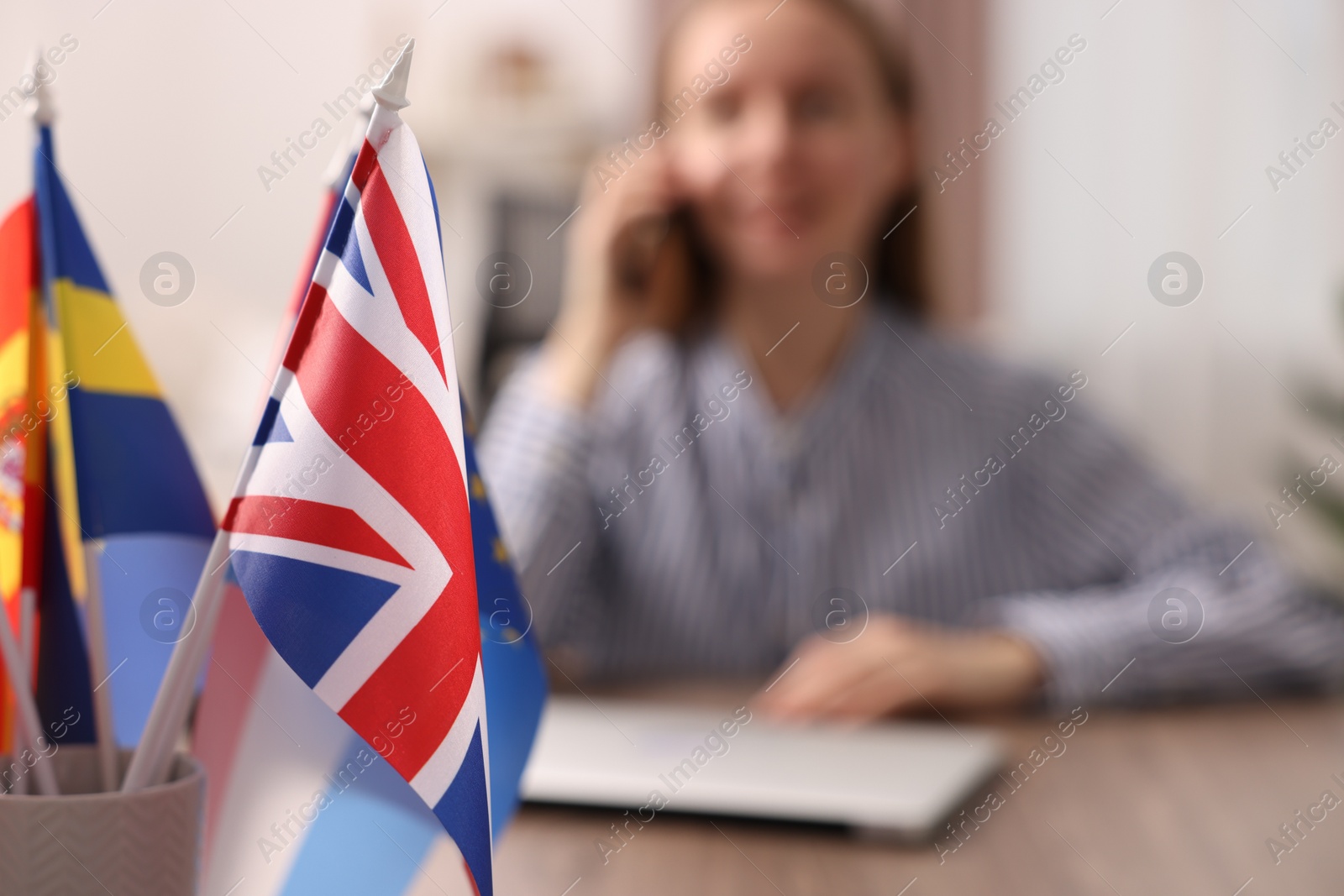 Photo of Woman talking on smartphone at table indoors, focus on different flags