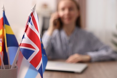 Photo of Woman talking on smartphone at table indoors, focus on different flags
