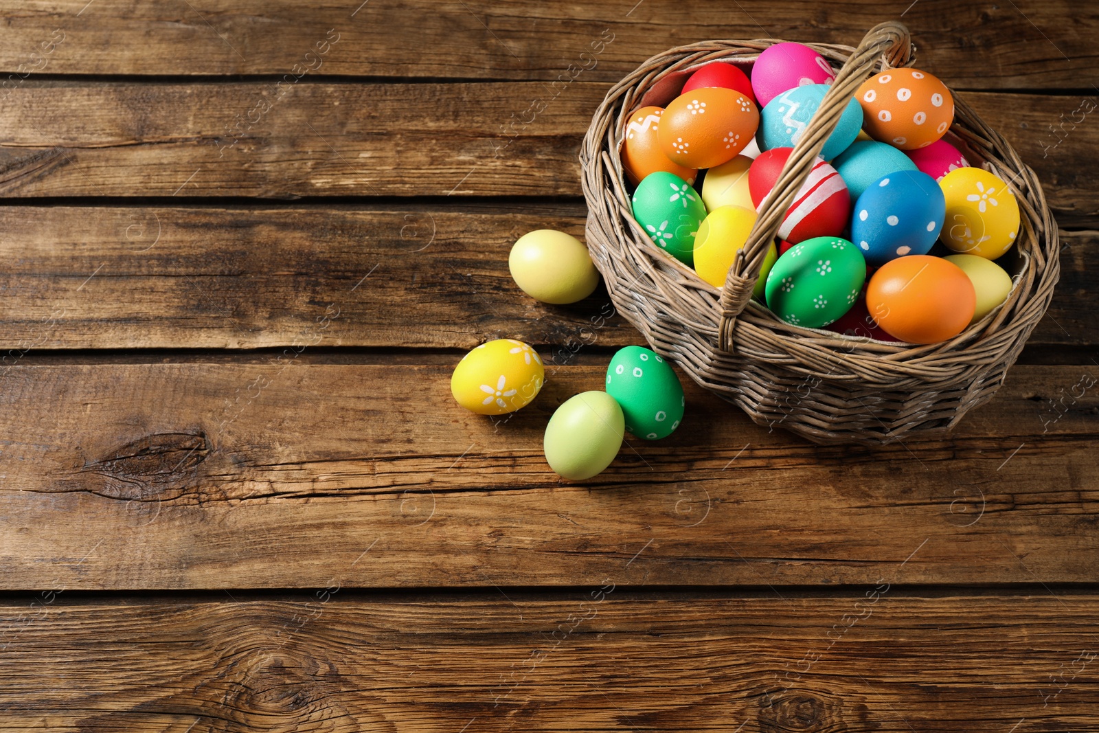 Photo of Colorful Easter eggs in basket on wooden background. Space for text