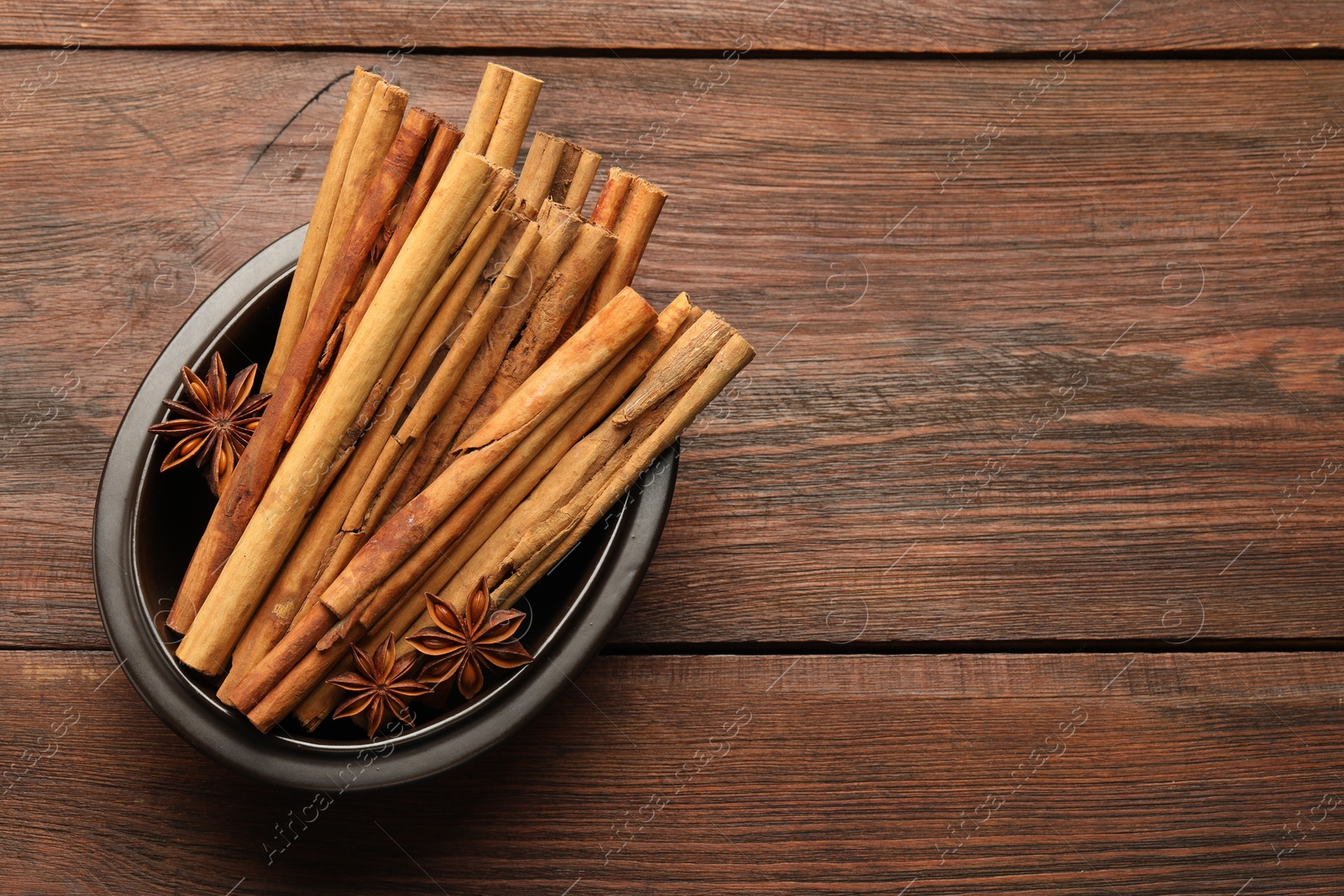 Photo of Bowl with cinnamon sticks and star anise on wooden table, top view. Space for text