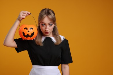 Photo of Woman in scary maid costume with pumpkin bucket on orange background, space for text. Halloween celebration