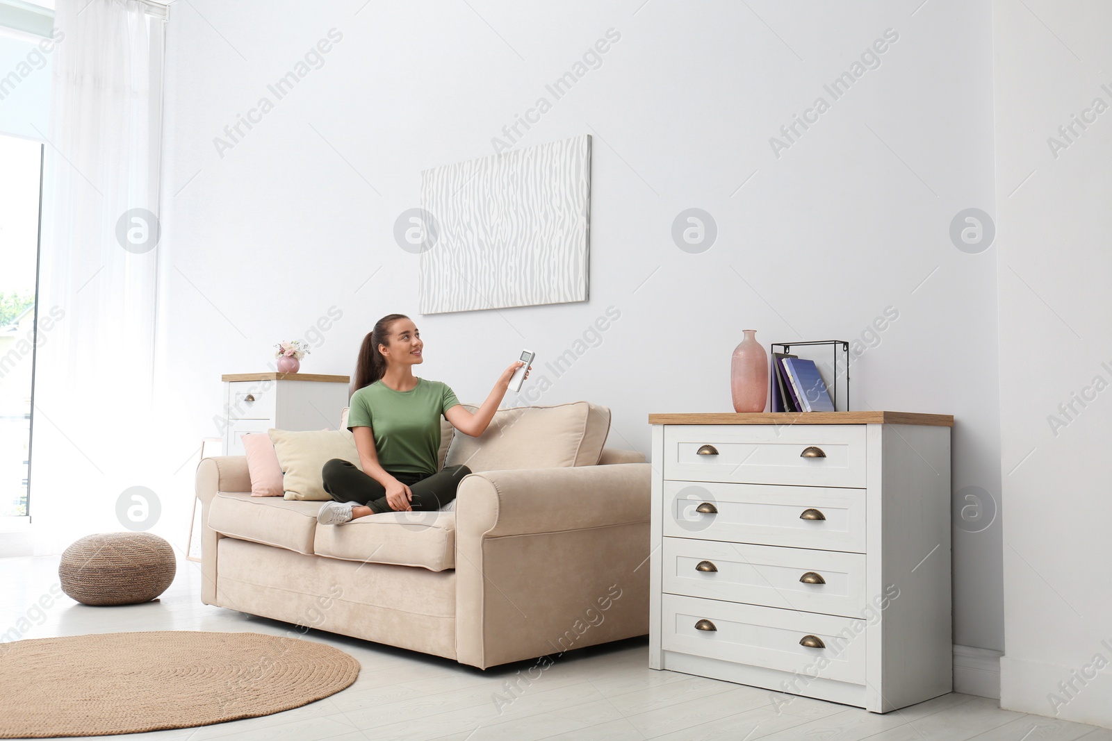 Photo of Happy young woman switching on air conditioner with remote control at home