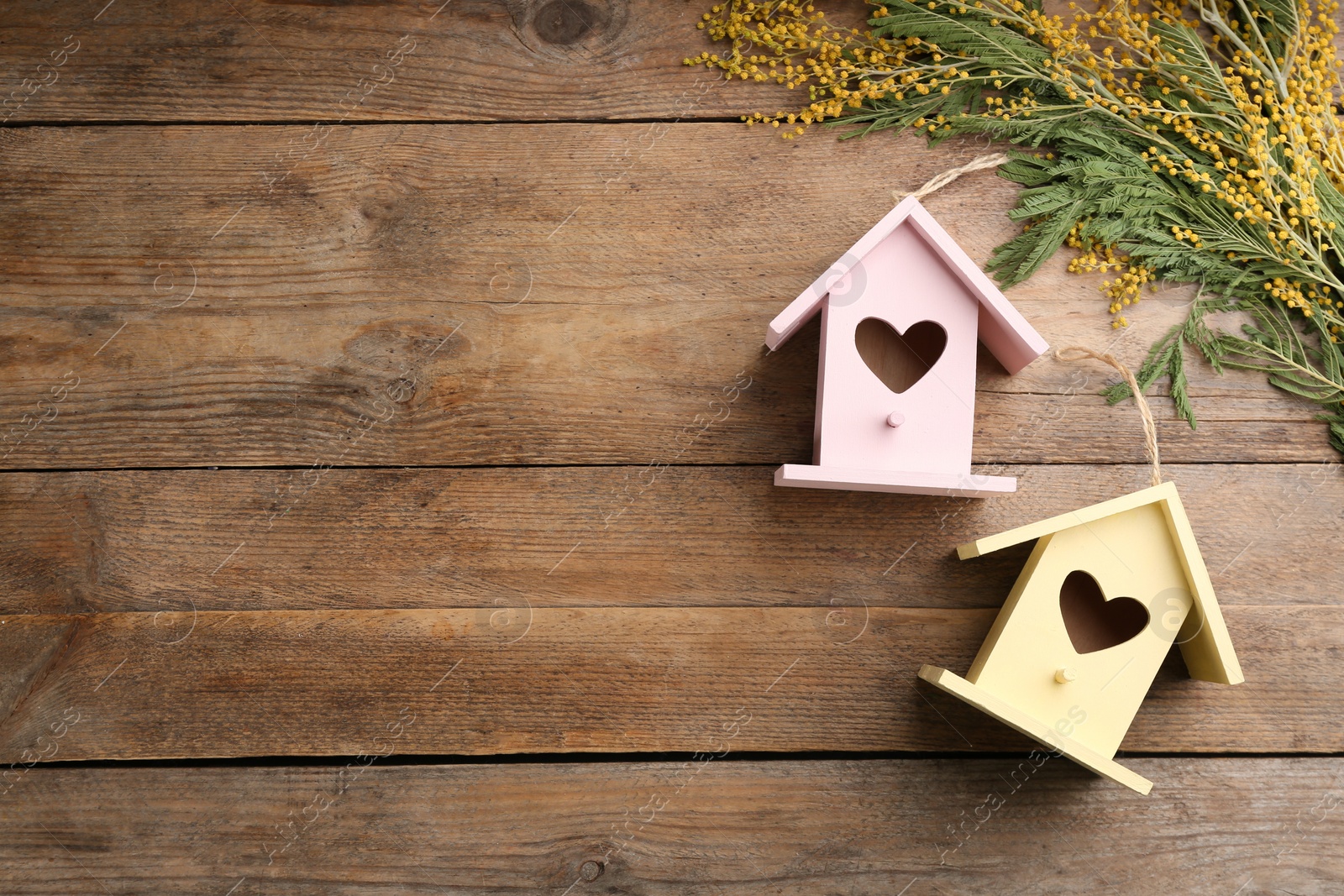 Photo of Beautiful bird houses with heart shaped holes and mimosa flowers on wooden background, space for text. Spring flat lay composition