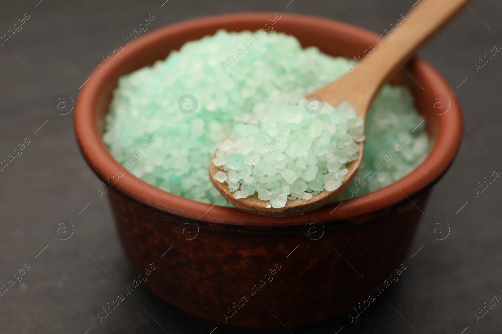 Photo of Bowl and spoon with turquoise sea salt on black table, closeup