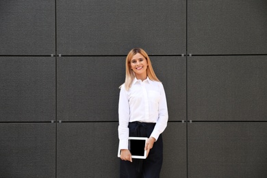 Female real estate agent with blank tablet near dark wall