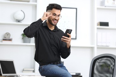 Photo of Happy young man using smartphone in office