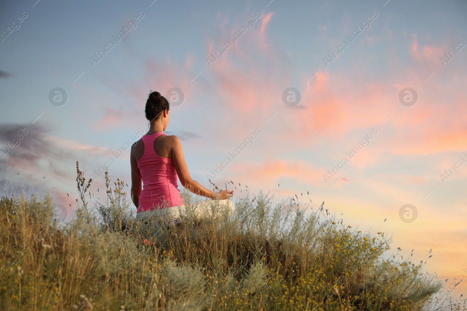 Photo of Woman meditating in meadow, back view. Space for text