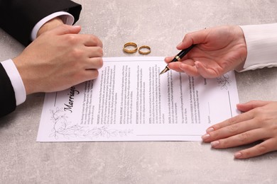 Photo of Man and woman signing marriage contract at light grey table, closeup