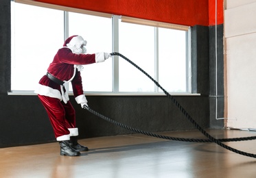 Young Santa Claus training with ropes in modern gym