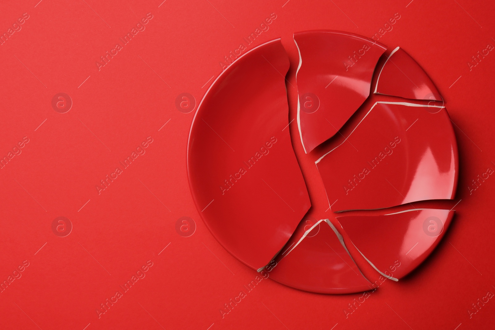 Photo of Pieces of broken ceramic plate on red background, top view. Space for text