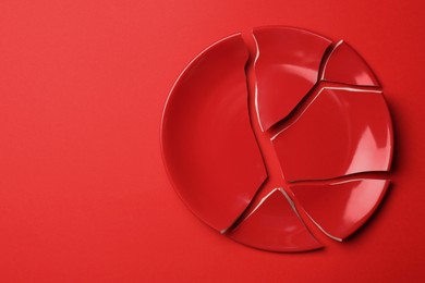 Pieces of broken ceramic plate on red background, top view. Space for text