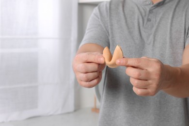 Photo of Man holding tasty fortune cookie with prediction indoors, closeup. Space for text