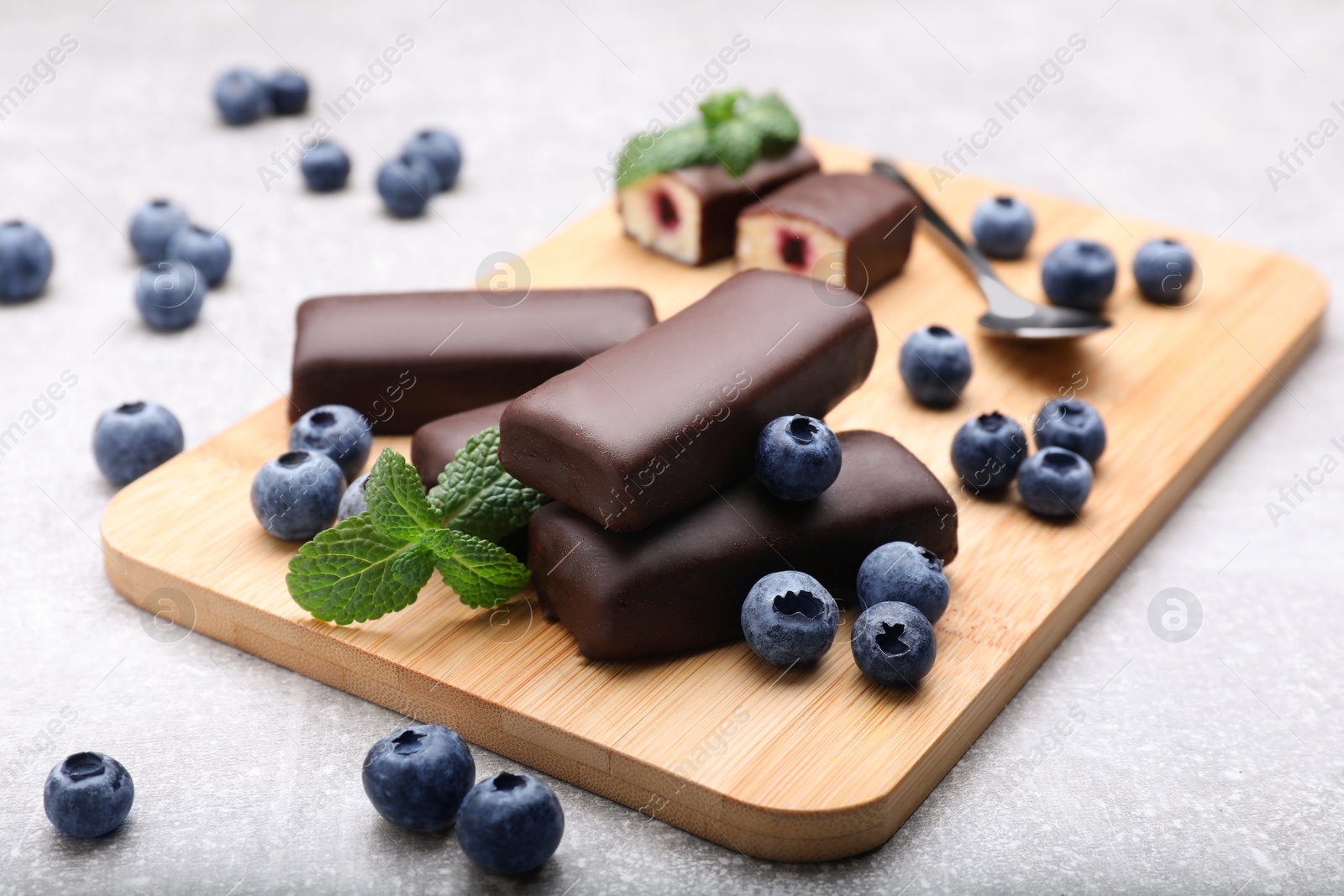 Photo of Delicious glazed curd snacks with fresh blueberries and mint on light grey table