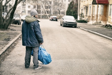 Poor homeless man with bag on city street