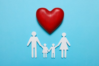 Photo of Paper family figures and red wooden heart on light blue background, flat lay. Insurance concept