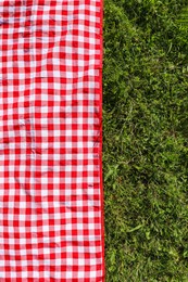 Checkered picnic tablecloth on fresh green grass, top view. Space for text