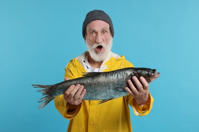 Photo of Shocked fisherman with caught fish on light blue background