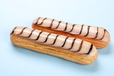 Photo of Delicious eclairs covered with glaze on light blue background