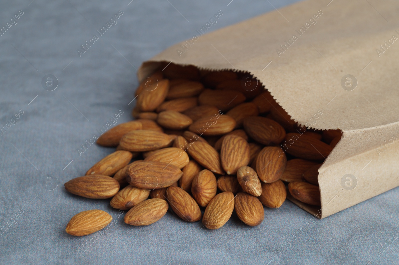 Photo of Paper bag with delicious almonds on grey table, closeup