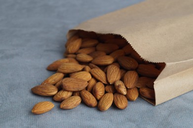 Photo of Paper bag with delicious almonds on grey table, closeup